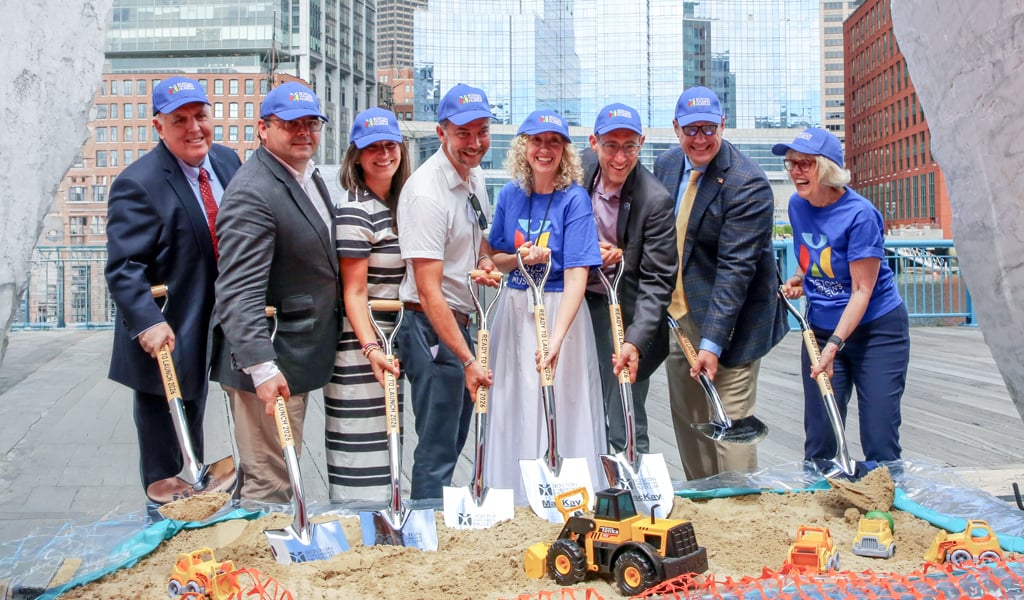 A group of individuals in business attire and blue caps are participating in a groundbreaking ceremony.  