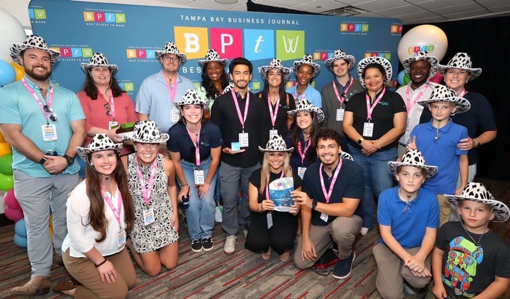A group of coworkers stand in front of a Best Places to Work banner.