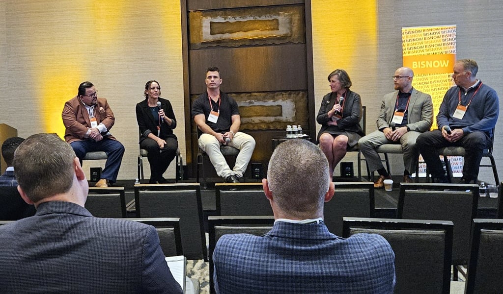 Panel discussion at a Bisnow event featuring five speakers seated in front of an audience.