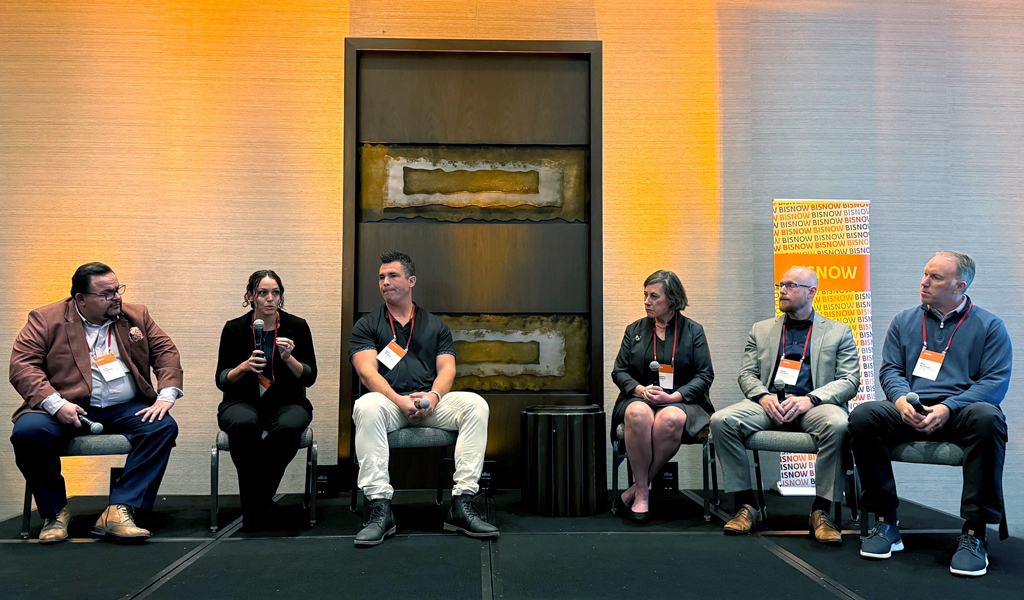 Panel discussion at a Bisnow event featuring five speakers seated in front of an audience.