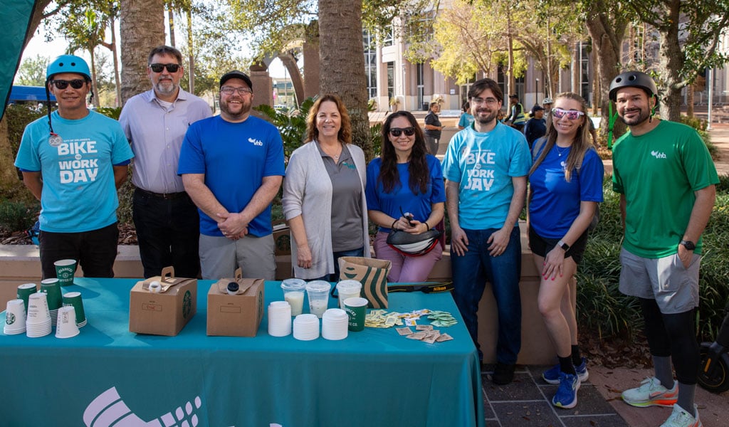2.	VHB Orlando team members stand behind a Bike to Work Day table with refreshmentsin a downtown park.
