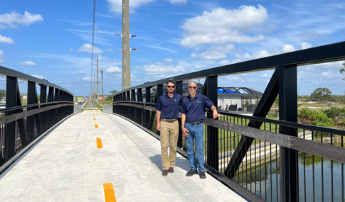 Marc Bertoncini and Kenneth Ray stand on a multimodal trail bridge over a canal 