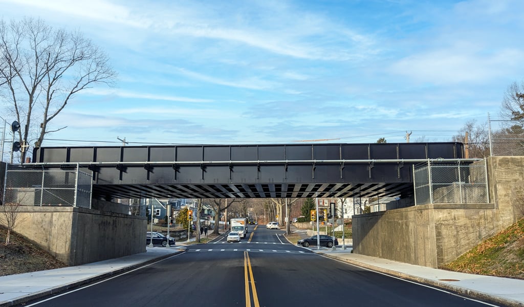 A road passes beneath a steel bridge with concrete supports on either side.  