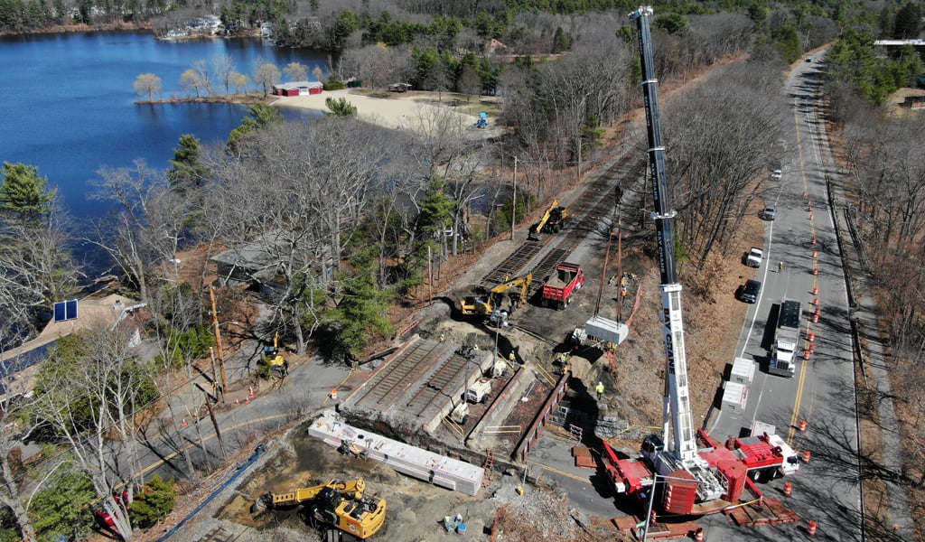 A construction site next to a lake. Heavy machinery, including cranes and excavators, are actively in use.