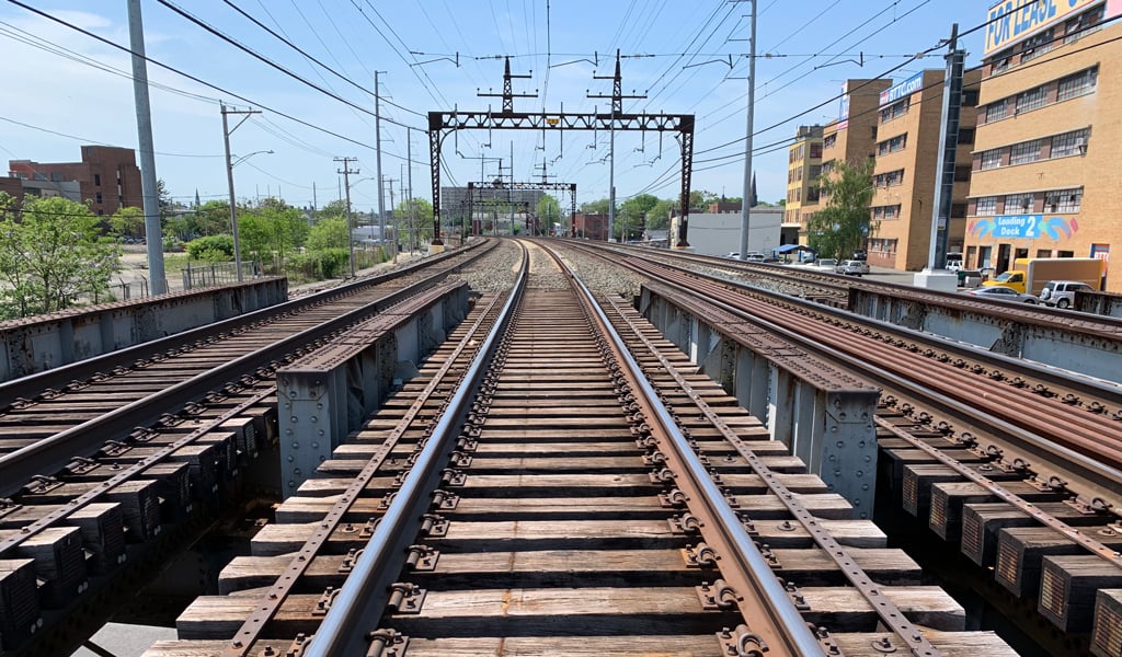 Railway tracks stretch into the distance, elevated on a bridge. Overhead power lines run parallel to the tracks. 