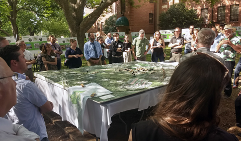 Community members gather around a park model for a presentation of the future Dix Park.