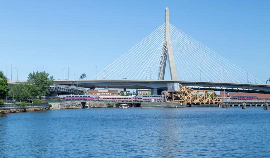 A train crossing a draw bridge, beneath a suspension bridge