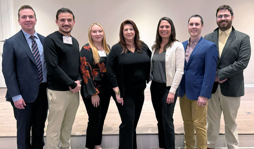 Seven people smiling and standing together, facing the camera.