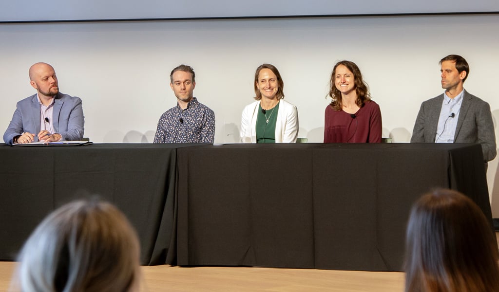 A panel of five individuals is seated at a long table covered with a black tablecloth.  