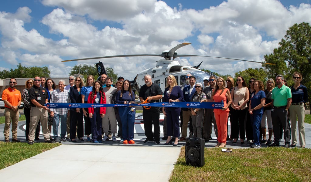 The project team smiling and getting ready to cut the ribbon on the new helipad in front of a helicopter. 