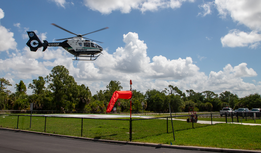 Helicopter flying over green grass to land on the new helipad at HCA Florida Englewood Hospital.
