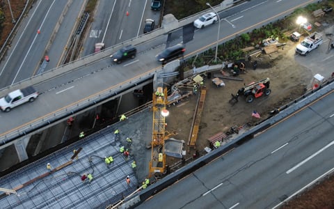 Aerial view of a construction site on a highway bridge with workers, vehicles, and construction equipment.