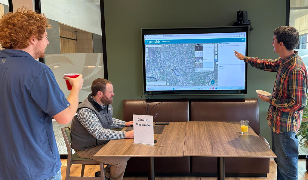 Three people point at a screen displaying GIS data.