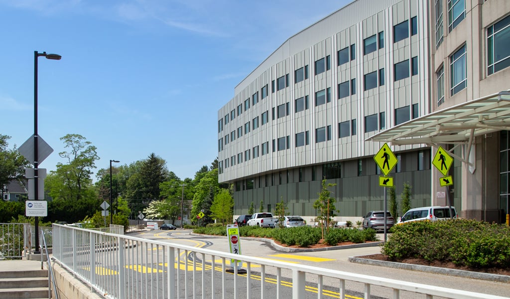 A five-story hospital with surrounding parking and a stairway to public transit station.