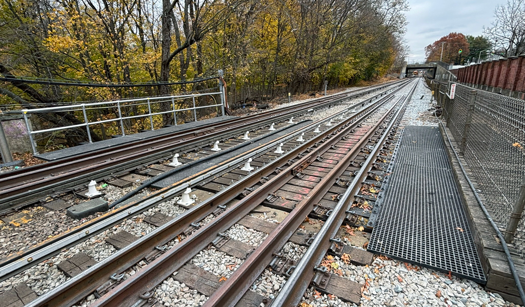 Railroad tracks extend into the distance with autumn-colored trees on either side and an overcast sky above.