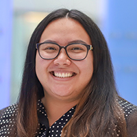 A person with long hair, wearing a black blouse with white polka dots.
