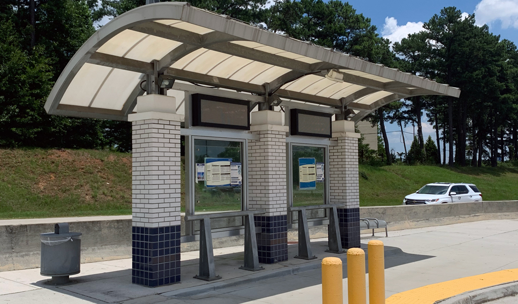 A photo of a modern covered bus stop with shade and maps for riders. 