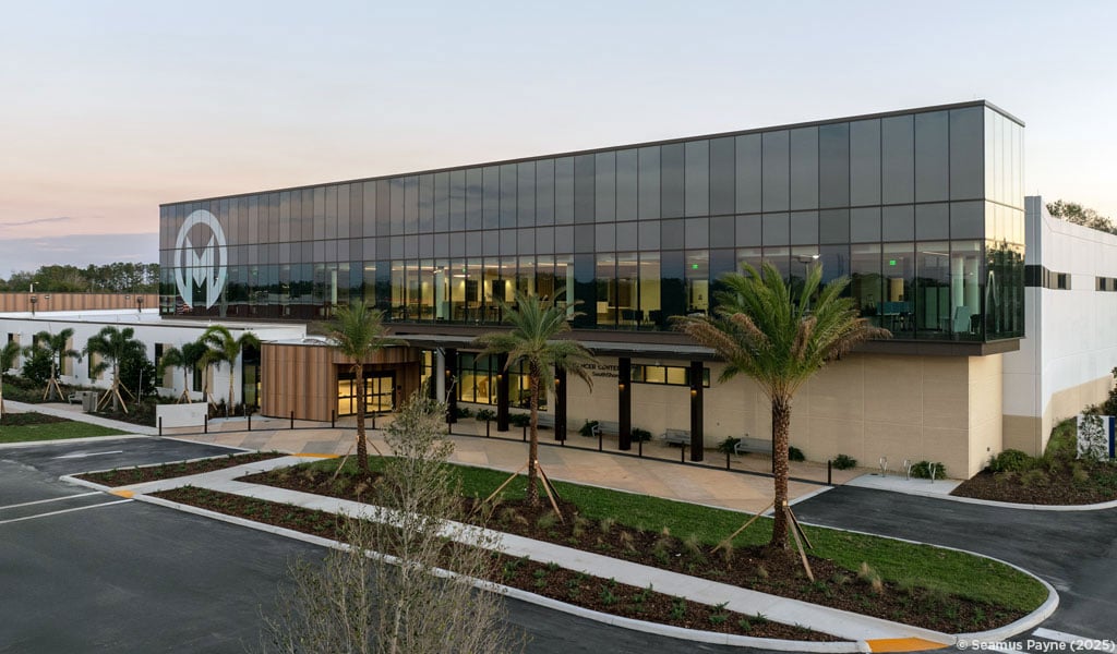 A modern healthcare facility in the evening with palm trees in front.