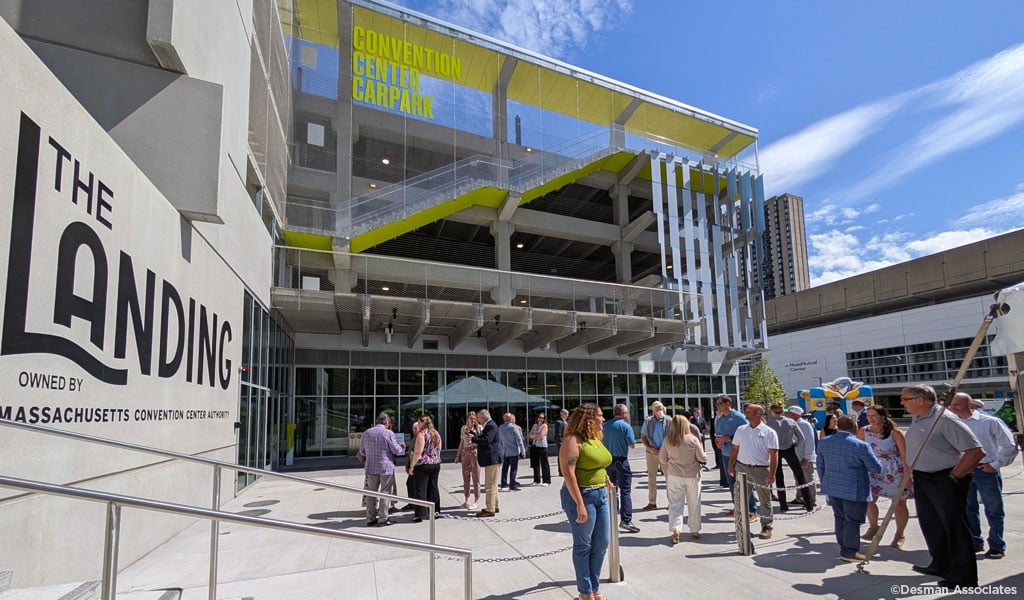 vA group of people stand outside the Massachusetts Convention Center. The building displays a sign reading "The Landing."