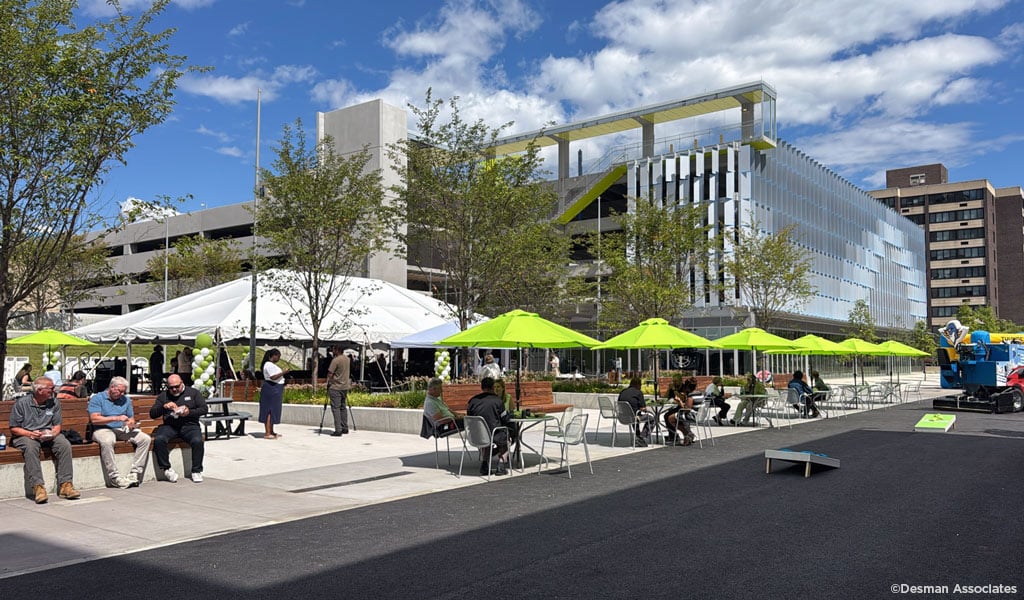 A lively outdoor scene at a parklet featuring people sitting at tables under bright green umbrellas.
