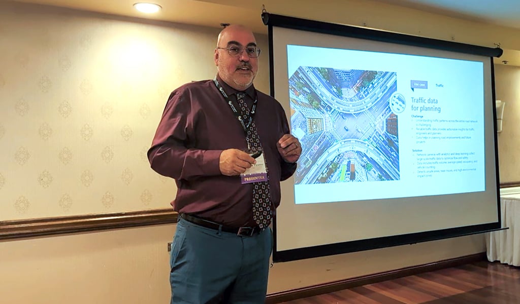 A person standing in a room gives a presentation next to a projected slide titled "Traffic data for planning" by Waze. 