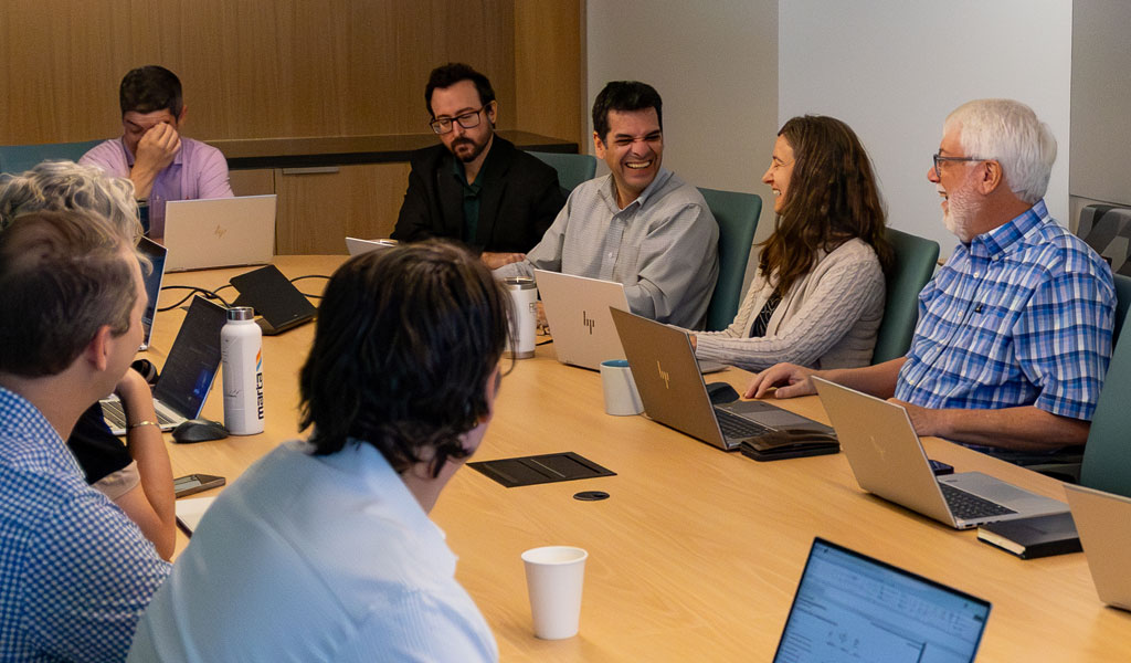 John Fish, wearing a blue plaid shirt, talking with his colleagues around a conference table.