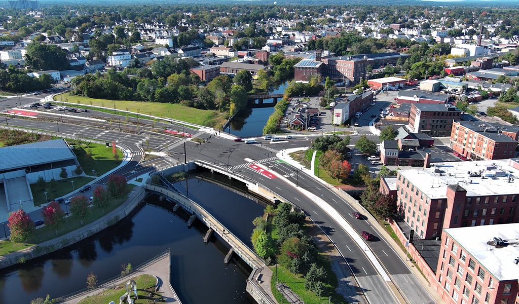 Aerial view of a cityscape featuring roads, a bridge over a river, and various buildings under a clear sky.