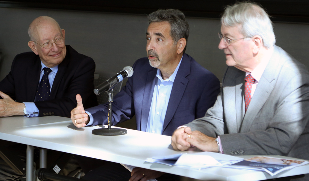 Three individuals participating in a panel discussion. The person in the center is speaking into a microphone, with another panelist on each side.