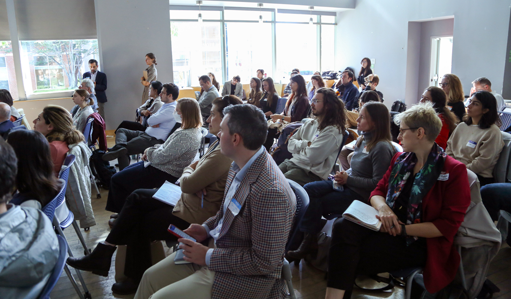Attendees seated in rows at a conference event inside a modern venue with large windows and natural light.
