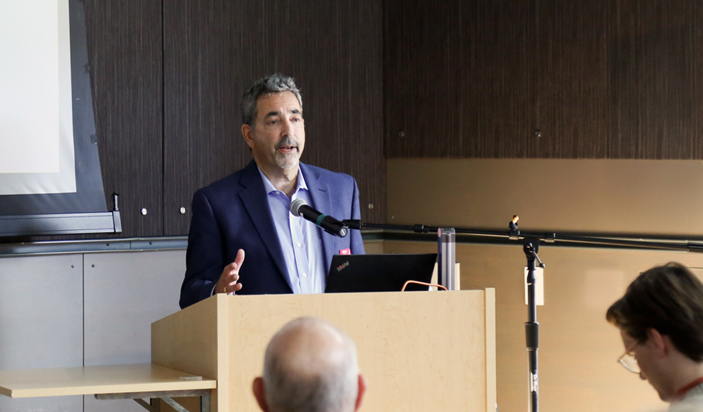 A person is giving a presentation at a podium in front of an audience in a conference room.