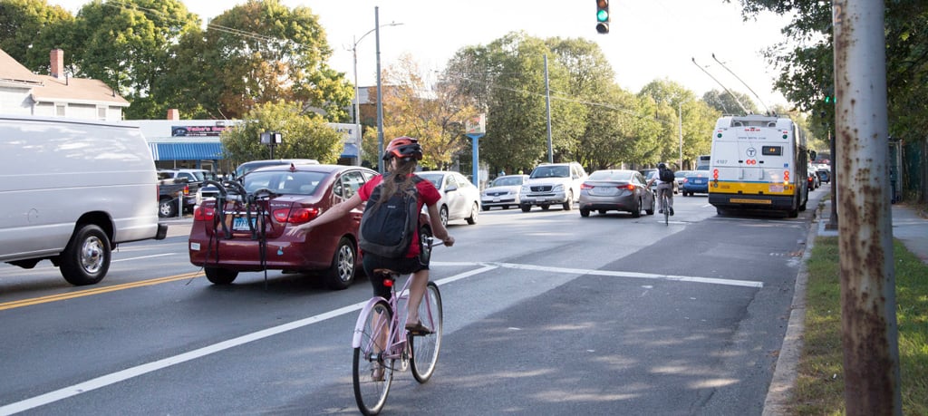 A cyclist uses hand signals to communicate with cars to change lanes.