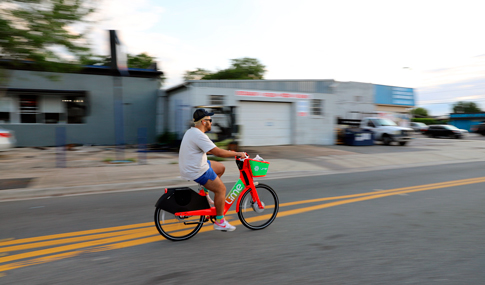 Man riding a Lime rental bike at dusk.