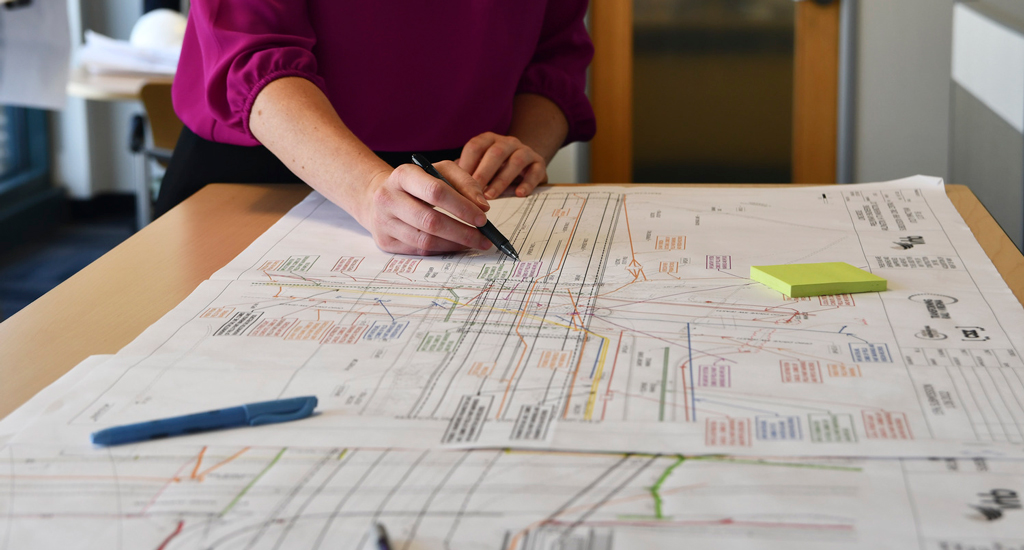 Woman in pink marks up a set of engineering plans.