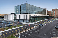 Modern hospital building with adjacent parking lots, crosswalks, and several parked vehicles.