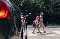 Car yields at a crosswalk as two young children cross the street. 