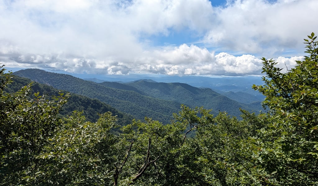 Scenic mountain views filled with green trees and a blue sky with clouds.