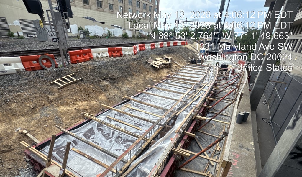 Crane and construction workers visible on railway and nearby roadway signs under a blue sky.