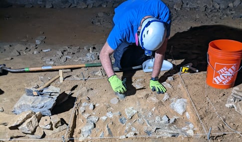 Josh Davis wearing a headlamp and gloves is bent over a test unit in Rafinesque Hall. 