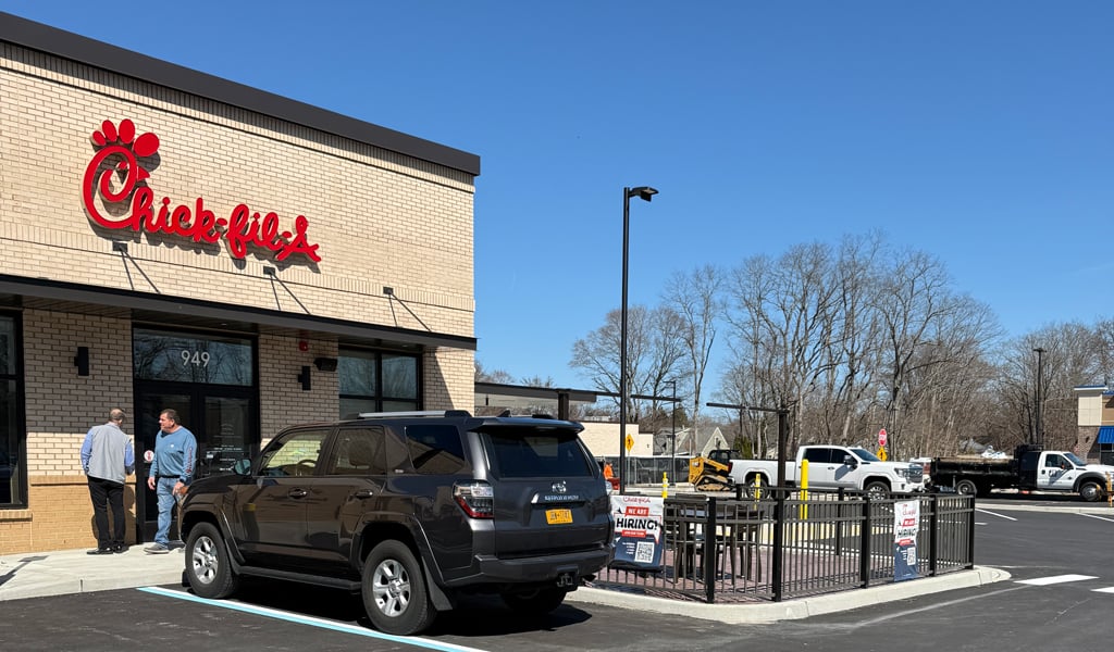 A view of Chick-fil-A’s front entry at the College Park Shopping Center with 2 cars parked.