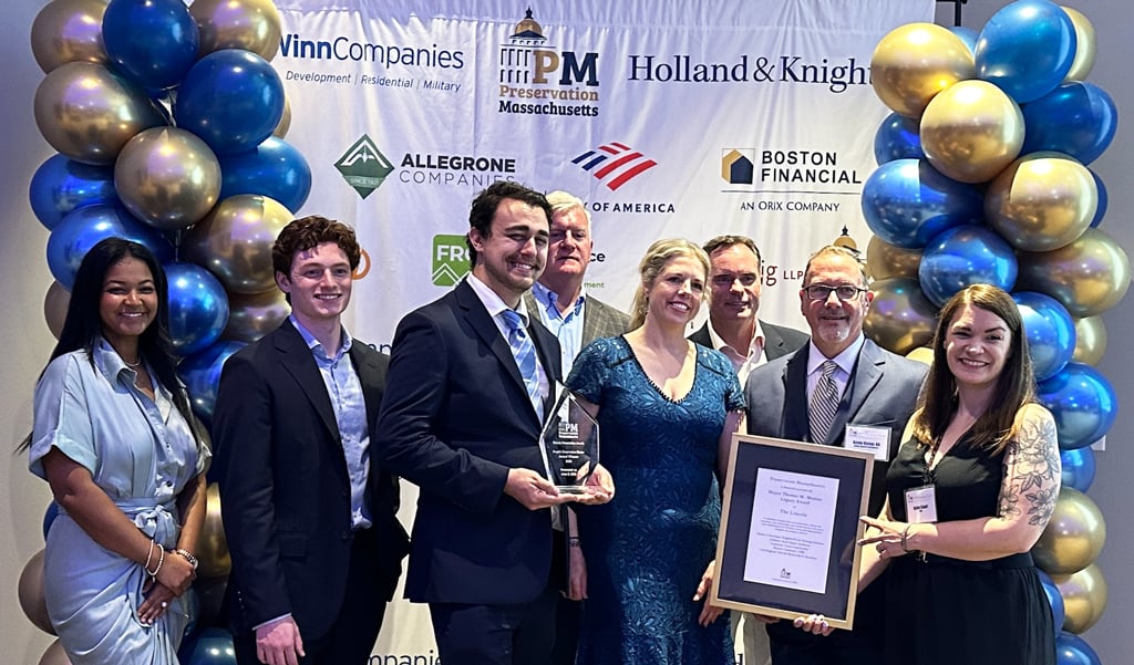 Group of people posing with an award at an event sponsored by WinnCompanies and others, standing in front of a balloon backdrop with company logos.