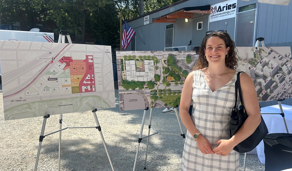 A person standing in front of three informational display boards showing urban development plans, with a building and American flags in the background.