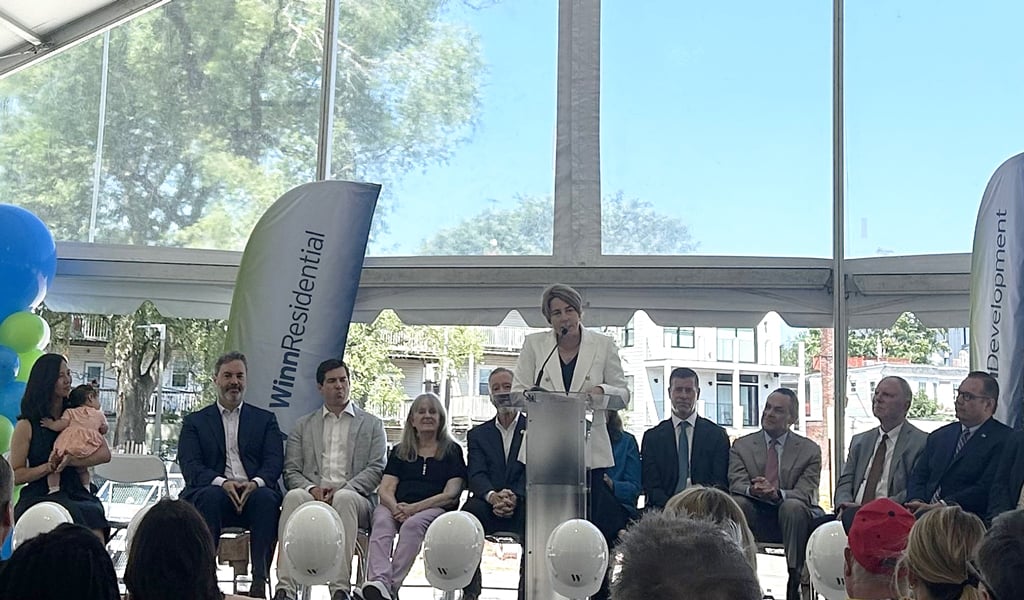 A person speaks at a podium with the WinnResidential logo on it, surrounded by seated individuals, under a large tent at a formal event.