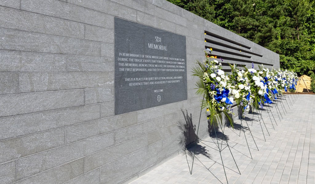 The gray stone memorial is lined with multiple blue floral arrangements.