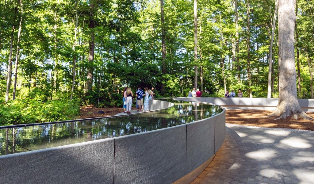 Winding water feature reflecting the green forest through the memorial.
