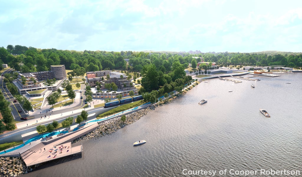 Aerial view of a waterfront development with modern buildings, a marina with several boats, and landscaped walkways.
