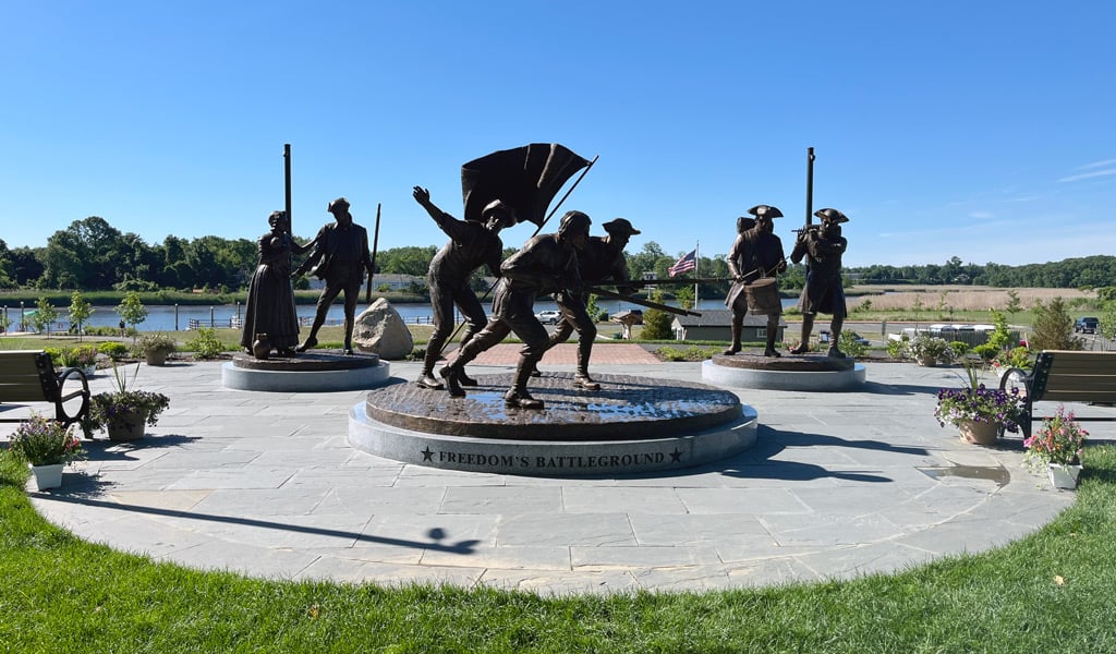 Outdoor monument titled "Freedom's Battleground," featuring bronze statues of soldiers and a woman arranged on circular stone platforms.