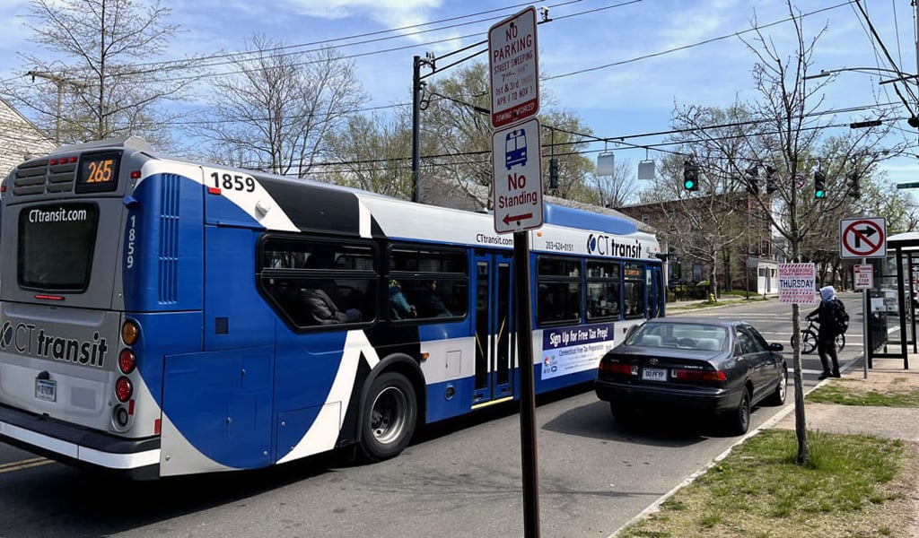 A bus stop sign with a blue-and-white CTtransit bus at an intersection in the background.