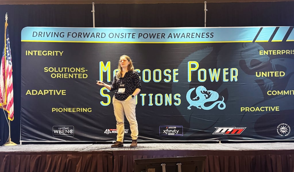 Person presenting on a podium with a banner reading "Mongoose Power Solutions" visible in background.