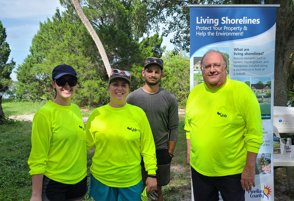 Neale Stralow and co-workers stand outdoors in front of a sign that reads living shoreline, a community volunteer oyster bed installation in Tampa Bay.