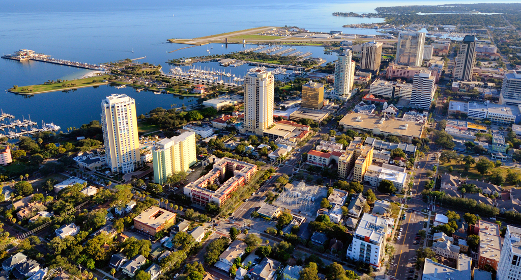 An aerial view of the city of St. Petersburg , Florida that shows large buildings beside a shoreline. 